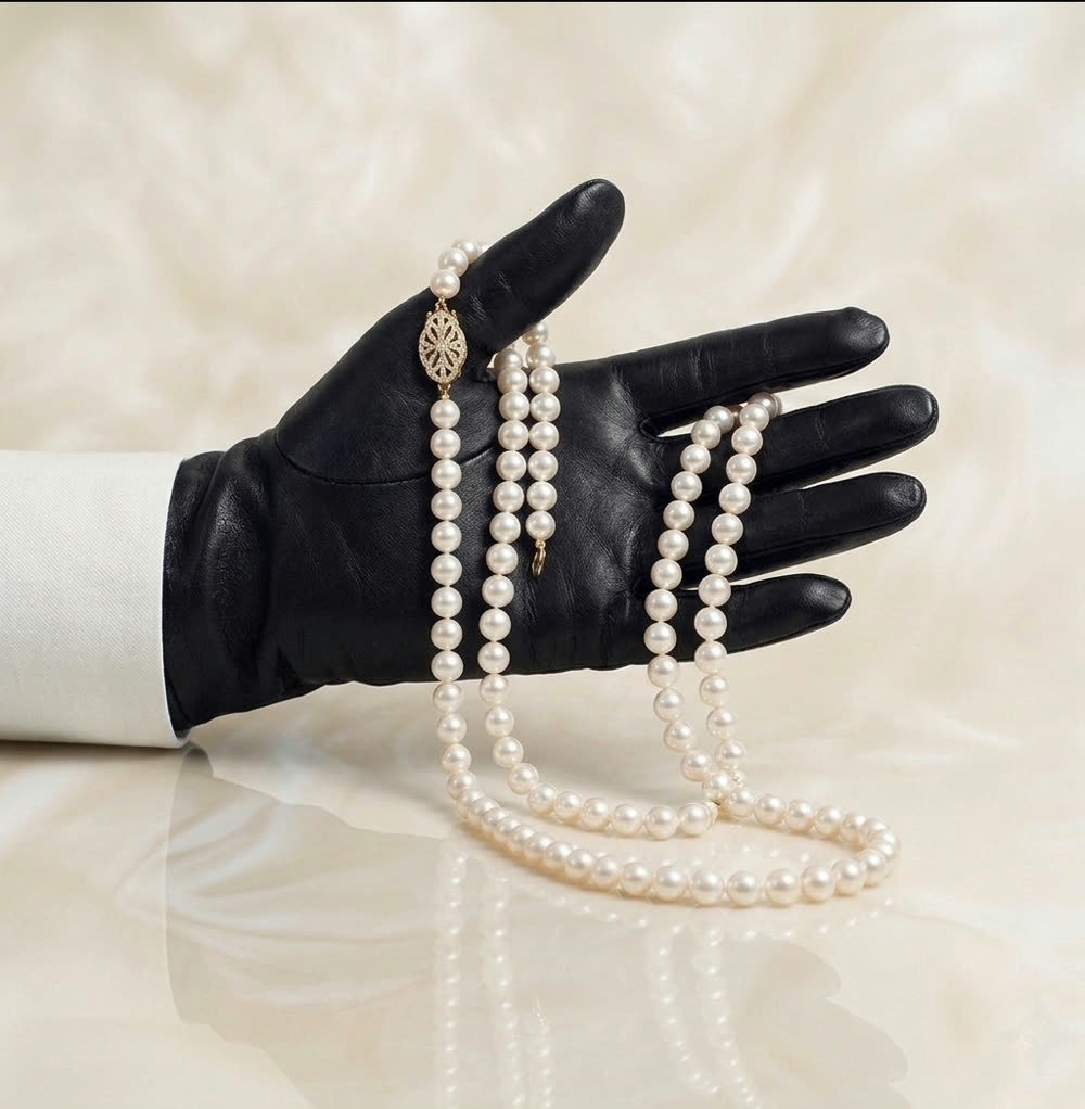 A gloved hand draped with strands of natural pearls